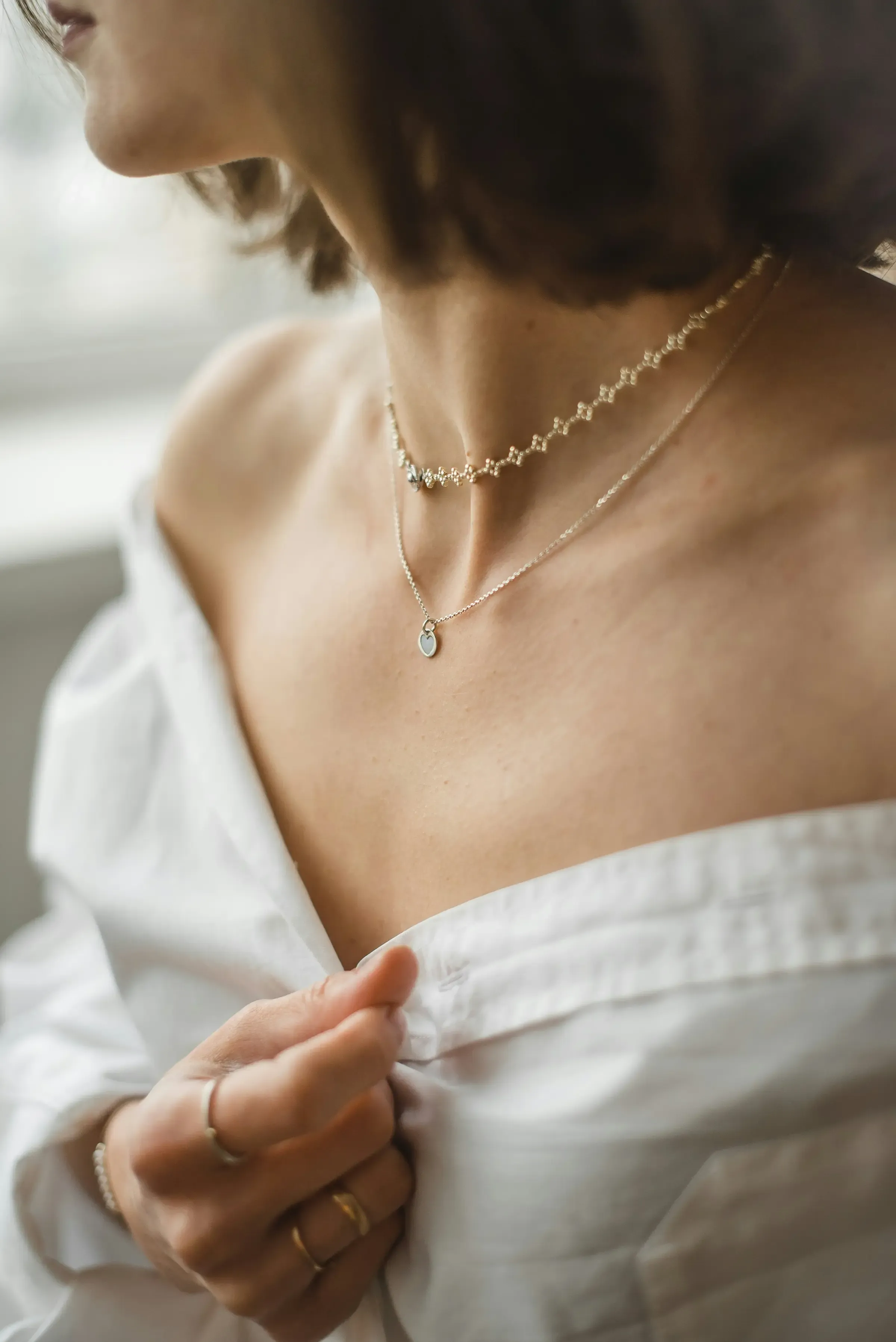 Femme portant des colliers superposés en or et des bagues fines