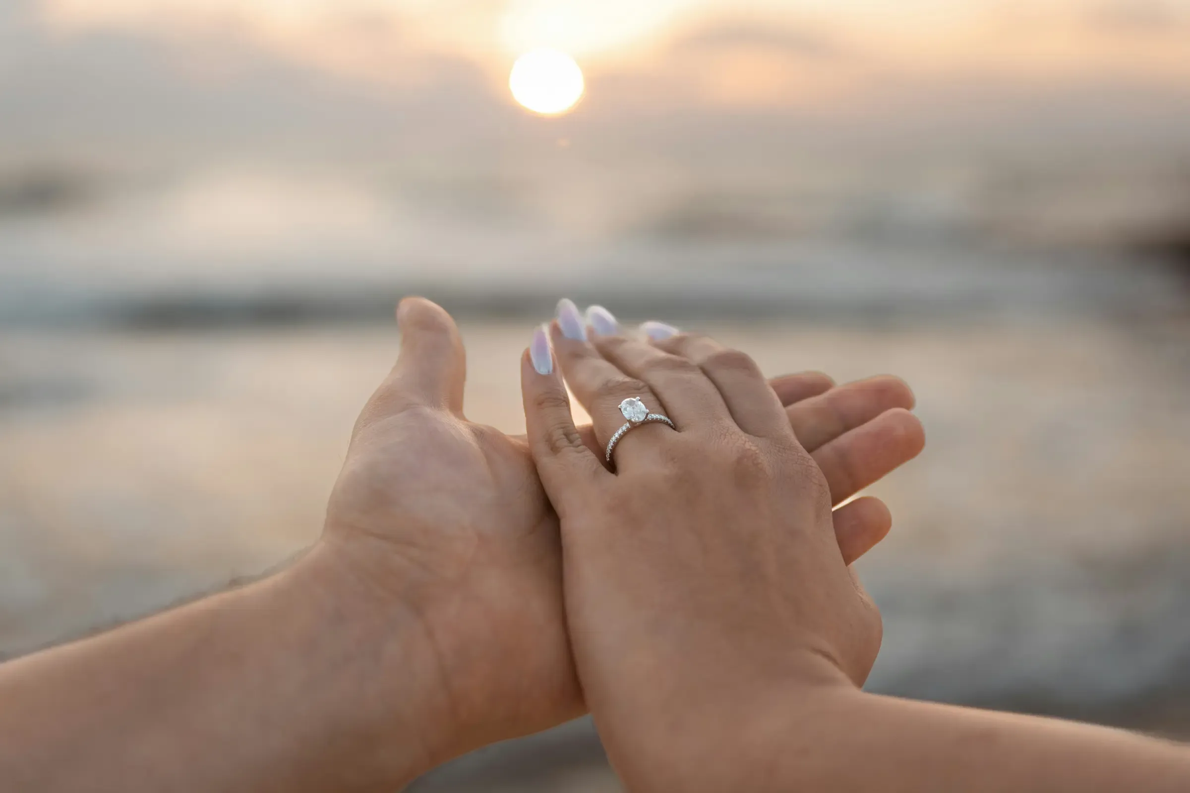 Main ornée d'une bague de fiançailles solitaire posée dans celle de son ou sa partenaire, au coucher du soleil